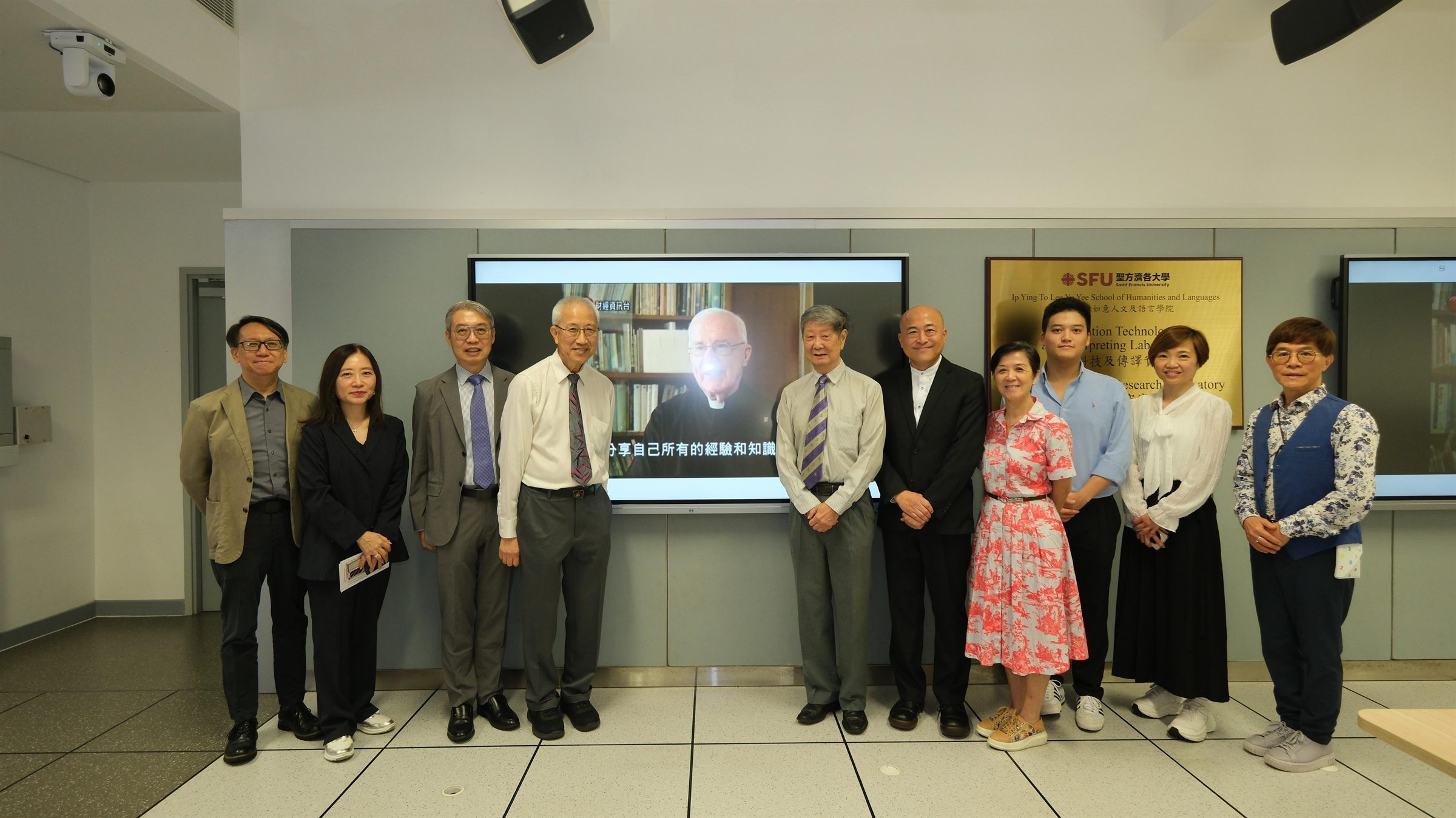 Ceremony guests gathered beside a screen showing Father Deignan